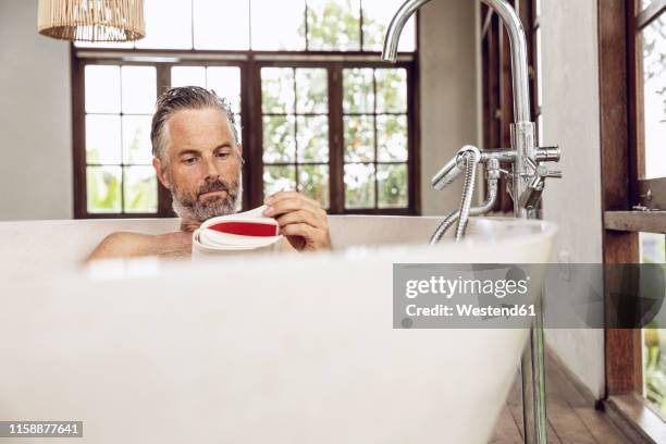 man reading book in bathtub - homem banho imagens e fotografias de stock