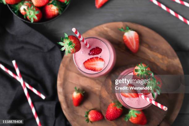 glasses of strawberry smoothie and strawberries on dark wood - strawberry smoothie stock pictures, royalty-free photos & images