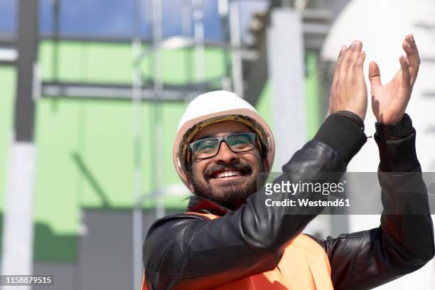 portrait of happy construction engineer in front of power station wearing hard hat and safety vest clapping hands - indian engineer stock-fotos und bilder