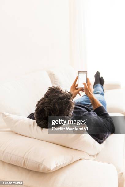 back view of young man lying on the couch at home using smartphone - auf rücken liegen stock-fotos und bilder