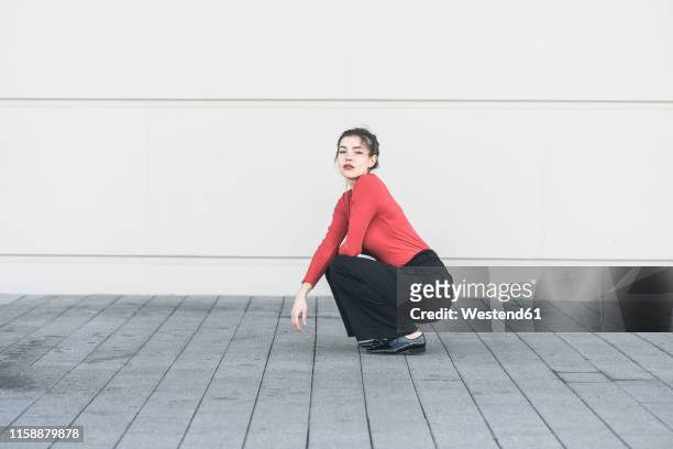 elegant young woman crouching in front of a wall - hockend stock-fotos und bilder