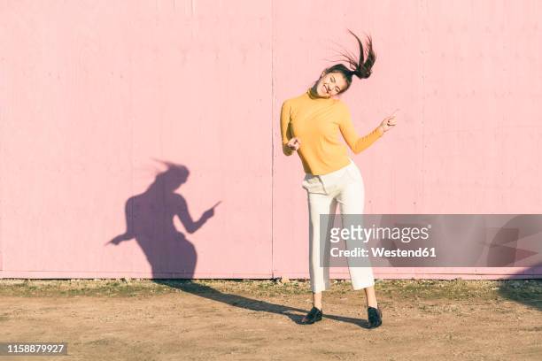 happy young woman dancing in front of a pink wall - joy stock-fotos und bilder