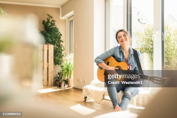 happy woman sitting at the window at home playing guitar - guitar player stock pictures, royalty-free photos & images