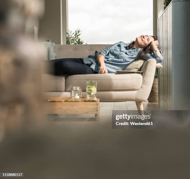 happy woman lying on the couch at home - couché de soleil photos et images de collection