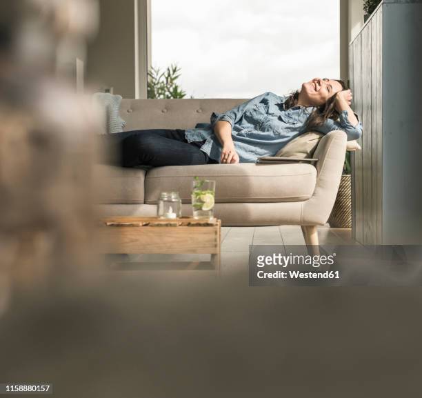 happy woman lying on the couch at home - comfortable couch stock pictures, royalty-free photos & images