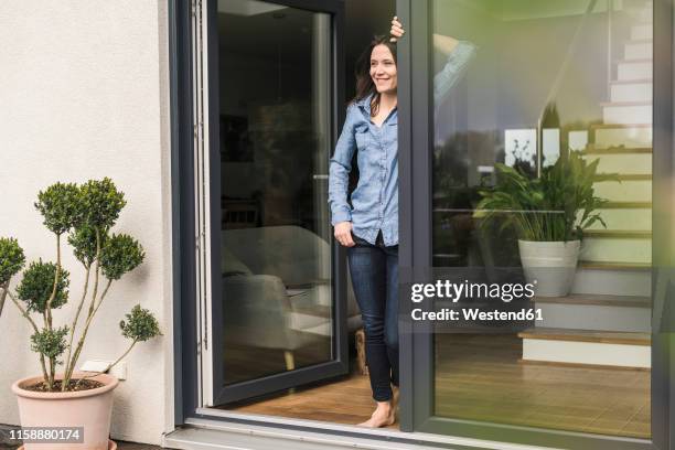 smiling woman standing at terrace door at home - french doors stockfoto's en -beelden