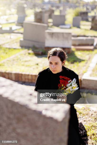 young woman, possibly a widow, carries flowers to a grave in a cemetery - widow stock pictures, royalty-free photos & images