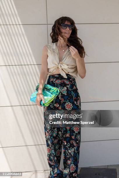 Guest is seen on the street attending 080 Barcelona Fashion Week wearing colorful floral pattern pants, taupe tied sleeveless top, metallic green bag...