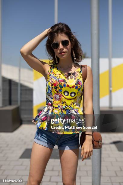 Guest is seen on the street attending 080 Barcelona Fashion Week wearing yellow with colorful pattern top, denim shorts, red shoes and aviator...