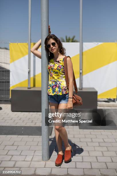 Guest is seen on the street attending 080 Barcelona Fashion Week wearing yellow with colorful pattern top, denim shorts, red shoes and aviator...