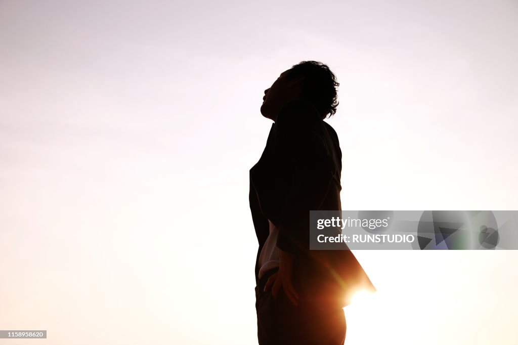Silhouette businessman looking up against sky at sunset