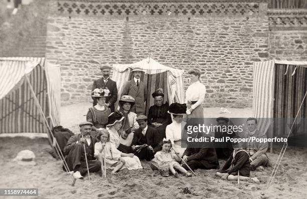 Family group wearing their Sunday best sitting on the sand at a beach in France, circa 1910.