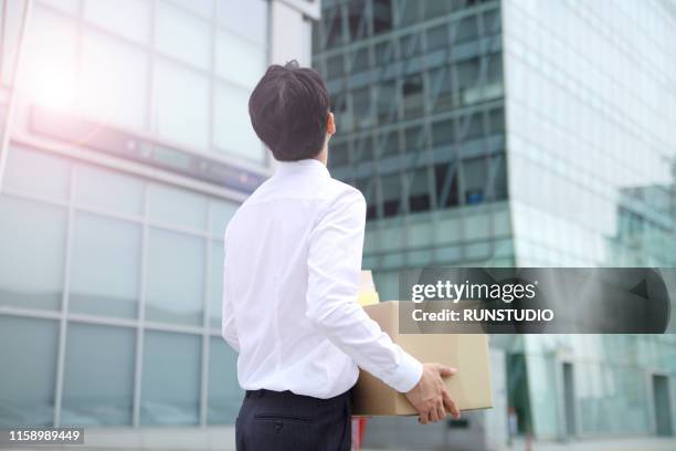 fired businesswoman standing with cardboard box outside office - moving office stock pictures, royalty-free photos & images