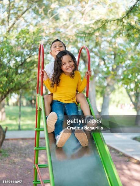 nettes kleines mädchen mit ihrem bruder auf einer rutsche zusammen - rutsche stock-fotos und bilder