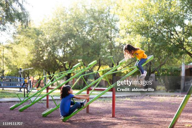 sisters playing on a seesaw together - public park playground stock pictures, royalty-free photos & images