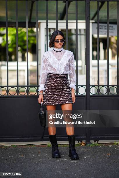 Bruna Marquezine wears earrings, a white lace embroidered top, a skirt, a balck bag with fringes, black boots, a small bow tie, outside Miu Miu Club...