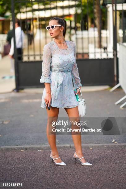 Adele Exarchopoulos wears sunglasses, a pale blue floral print dress, silver shoes, a necklace, earrings, outside Miu Miu Club 2020, on June 29, 2019...