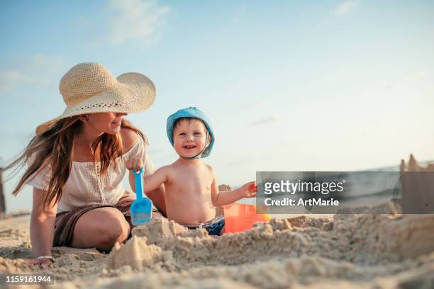 mère et fils sur la plage jouant avec le sable - château de sable photos et images de collection