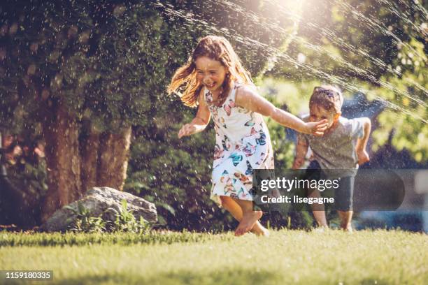glückliche kinder spielen mit garten sprinkler - spaß stock-fotos und bilder