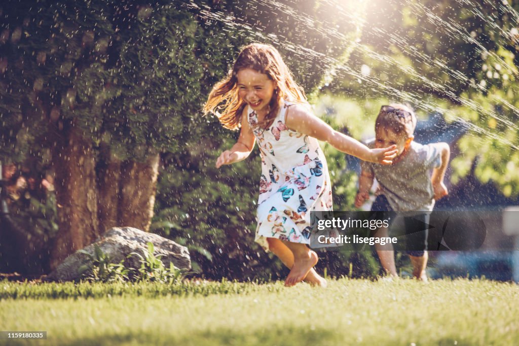 Bambini felici che giocano con l'irrigatore da giardino
