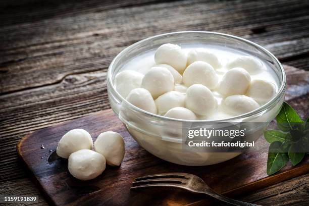 italienischeküche: mozzarella bocconcini in einer glasschüssel auf rustikalem holztisch - mozzarella stock-fotos und bilder