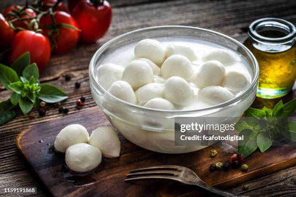 italienischeküche: mozzarella bocconcini in einer glasschüssel auf rustikalem holztisch - mozzarella stock-fotos und bilder