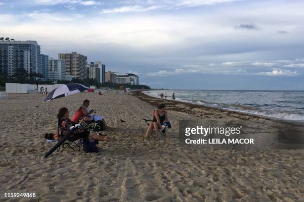 Maria Guadalupe Vazquez sits with her family in the shore of Miami Beach, Florida, on August 1, 2019. - Tons of this seaweed are upsetting tourists...