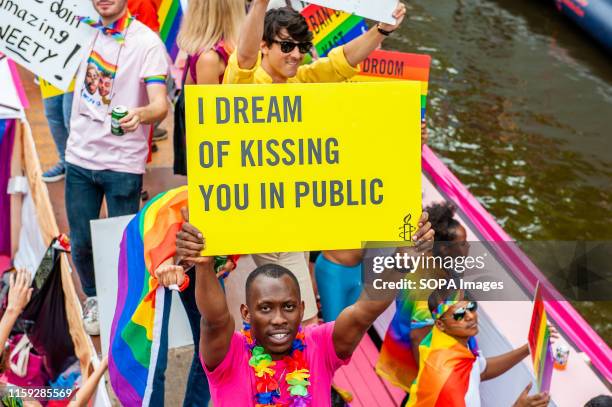 Black man holds a placard on the boat of Amnesty International during the parade. The Canal Parade is what Amsterdam Gay Pride is famous for. It's...