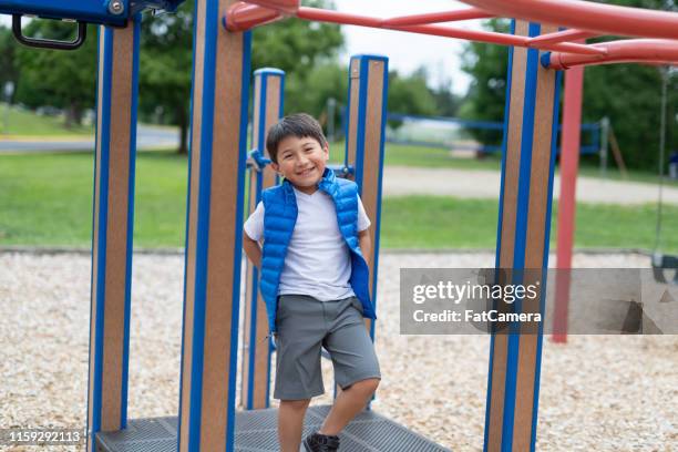 young boy smiling at the camera while he runs around a play structure - boy on monkey bars stock pictures, royalty-free photos & images