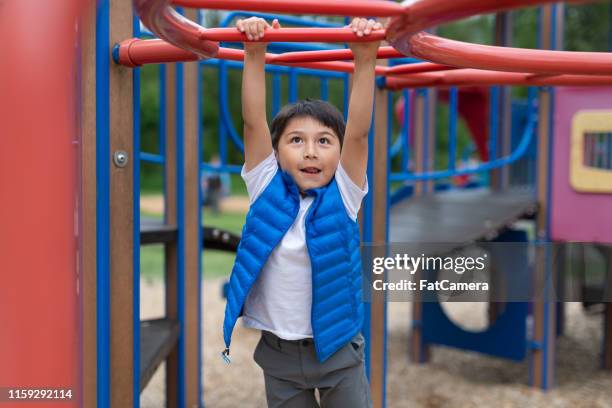 joven colgando de una estructura de juego en el patio de recreo - monkey bars fotografías e imágenes de stock