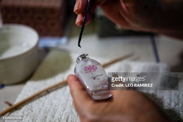 This picture taken on July 1, 2019 shows artist Zhang Yuhua painting a snuff bottle at her home in Beijing. - Delicate designs painted on the inside...