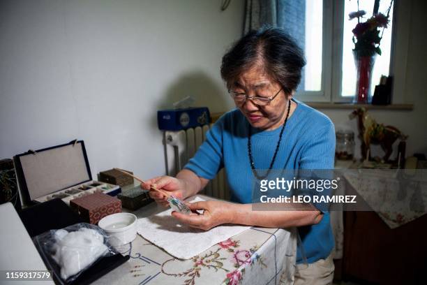 This picture taken on July 1, 2019 shows artist Zhang Yuhua painting a snuff bottle at her home in Beijing. - Delicate designs painted on the inside...