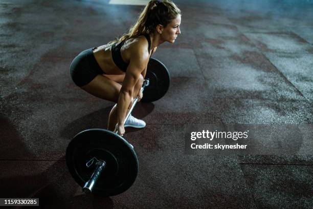 muscular build woman exercising deadlift with barbell in a health club. - deadlift stock pictures, royalty-free photos & images