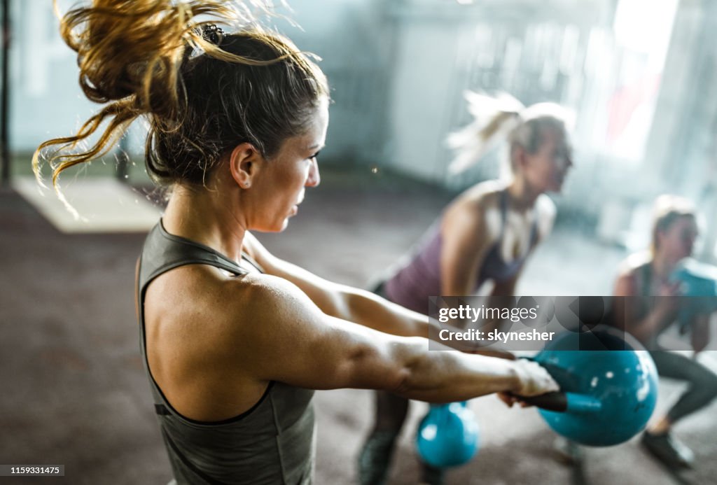Athletic woman exercising with kettle bell on a class in a health club.