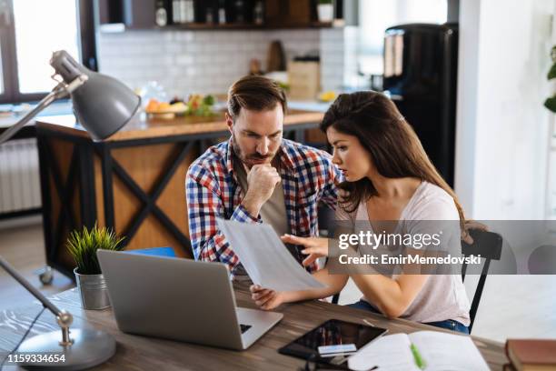 pareja frustrada revisando facturas en casa usando computadora portátil - financiación fotografías e imágenes de stock