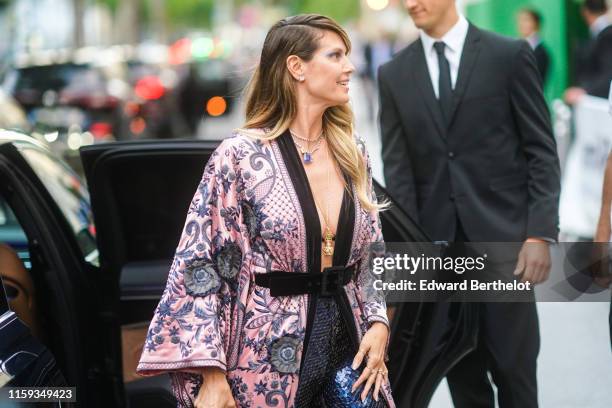 Heidi Klum wears earrings, necklaces, a lustrous beaded and embroidered floral print pale-pink kimono-style long jacket, a black velvet belt,...