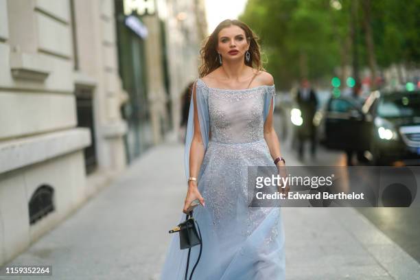 Guest wears earrings, a pale blue off- shoulder long flowing dress with glittering silver embroideries, a black bag , outside AMFAR dinner, during...
