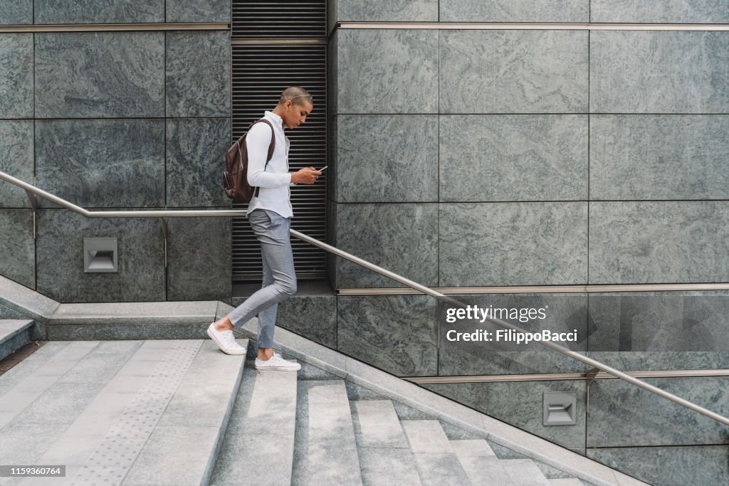 Ung vuxen affärs man i staden går ner för trapporna med smart telefon