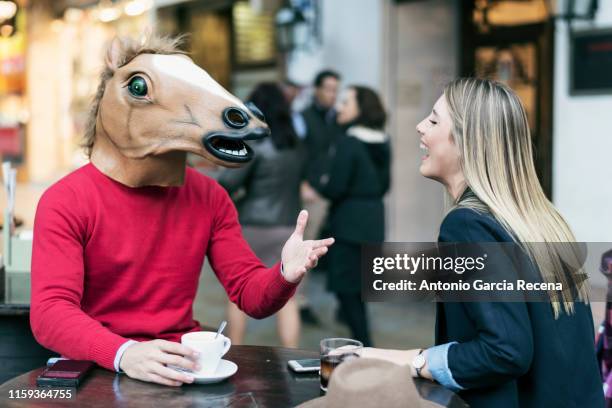 woman and horse face man with costume drinking coffee in bar terrace and talking having fun - außenseiter stock-fotos und bilder