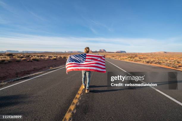man on road holding american flag - flags great america stock pictures, royalty-free photos & images