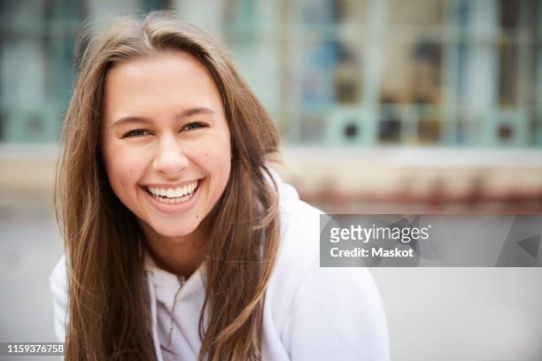 portrait of smiling teenage girl sitting in schoolyard - blonde girl smiling stock-fotos und bilder