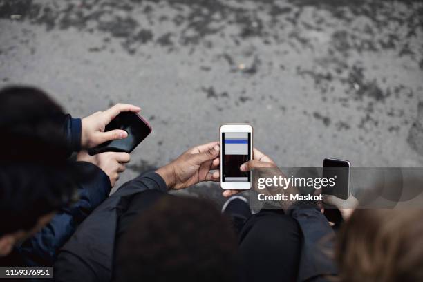 high angle view of male friends using social media while sitting on street - 3 teenagers mobile outdoors stock-fotos und bilder