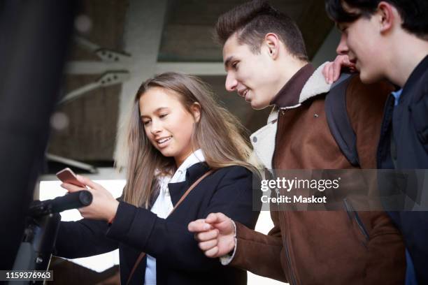 teenage boys looking at female friend using mobile phone below bridge - 3 teenagers mobile outdoors stockfoto's en -beelden