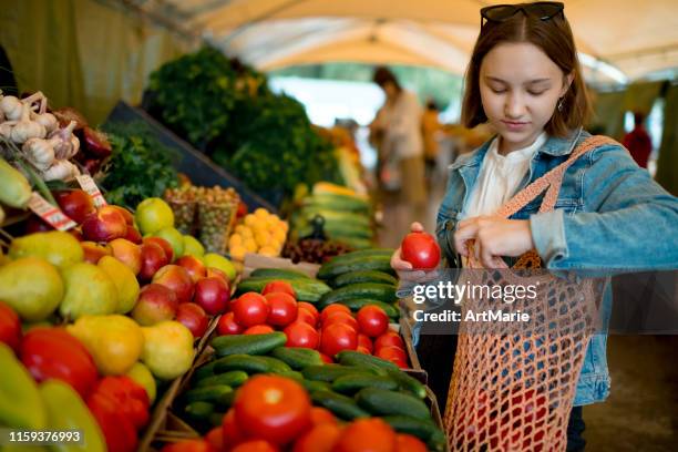 young girl choosing vegetables and fruit at a farmers market with reusable bag, plastic free and zero waste concept - plastic free stock pictures, royalty-free photos & images