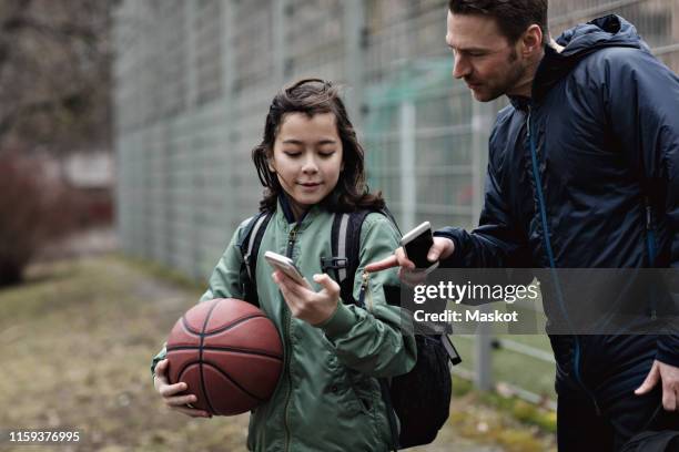 son showing mobile phone to father while standing on playing field in winter - season 13 stock-fotos und bilder