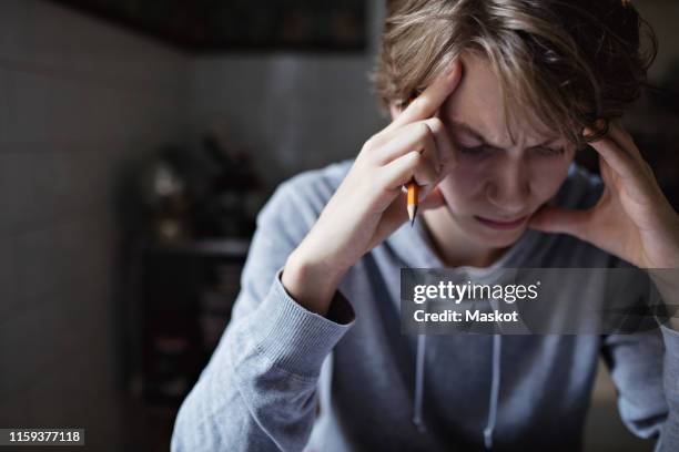 stressed teenage boy with head in hands studying at home - teenager headache stock pictures, royalty-free photos & images