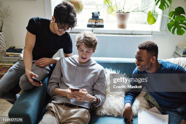 high angle view of social media addicted friends using smart phones on sofa during homework in living room - cell mates stock-fotos und bilder