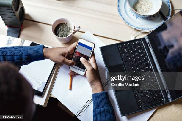 high angle view of teenage boy using mobile phone while studying on table at home - addiction mobile and laptop stock-fotos und bilder