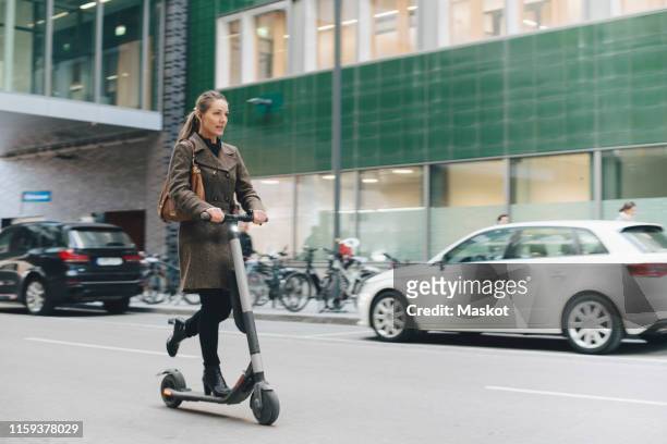 full length of confident businesswoman riding electric push scooter on street in city - scooter stock pictures, royalty-free photos & images