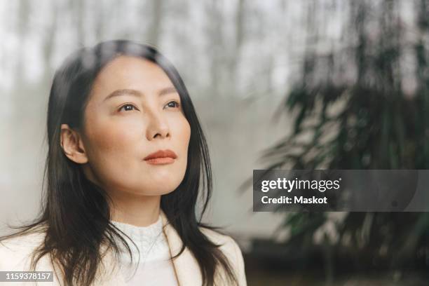 thoughtful mid adult businesswoman looking through window at office - asian man thinking stock-fotos und bilder